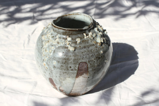This wheel thrown vase is decorated with black and white slip beneath a wood ash glaze and feldspar chips. It has an organically shaped rim that enhances the delicacy of the object. The bare clay body has been left exposed in places.